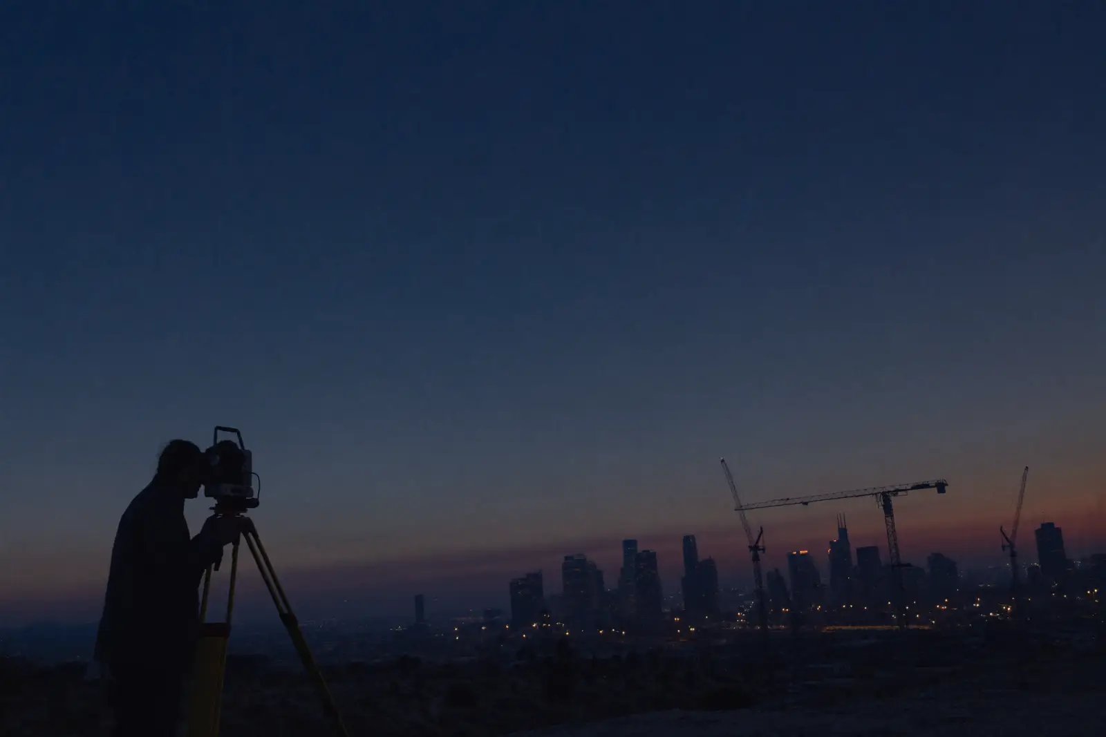 Surveyor at dusk overlooking a construction skyline